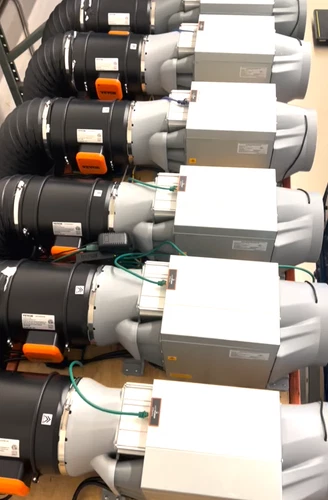 A rack of Antminer S19k Pro units with their power supplies mounted above them and white flexible ducting carrying exhaust air away from each machine.