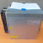 An Antminer L-series Scrypt unit on an orange service mat, silver chassis with its power supply fitted on top and a white label sheet resting on it, seen slightly from the left.