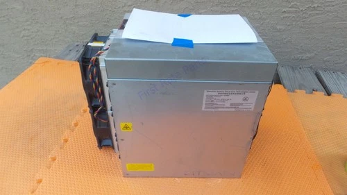 An Antminer L-series Scrypt unit on an orange service mat, silver chassis with its power supply fitted on top and a white label sheet resting on it, seen slightly from the right.