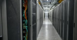 An aisle of grey server cabinets in a data hall, one cabinet open showing bundled fibre.