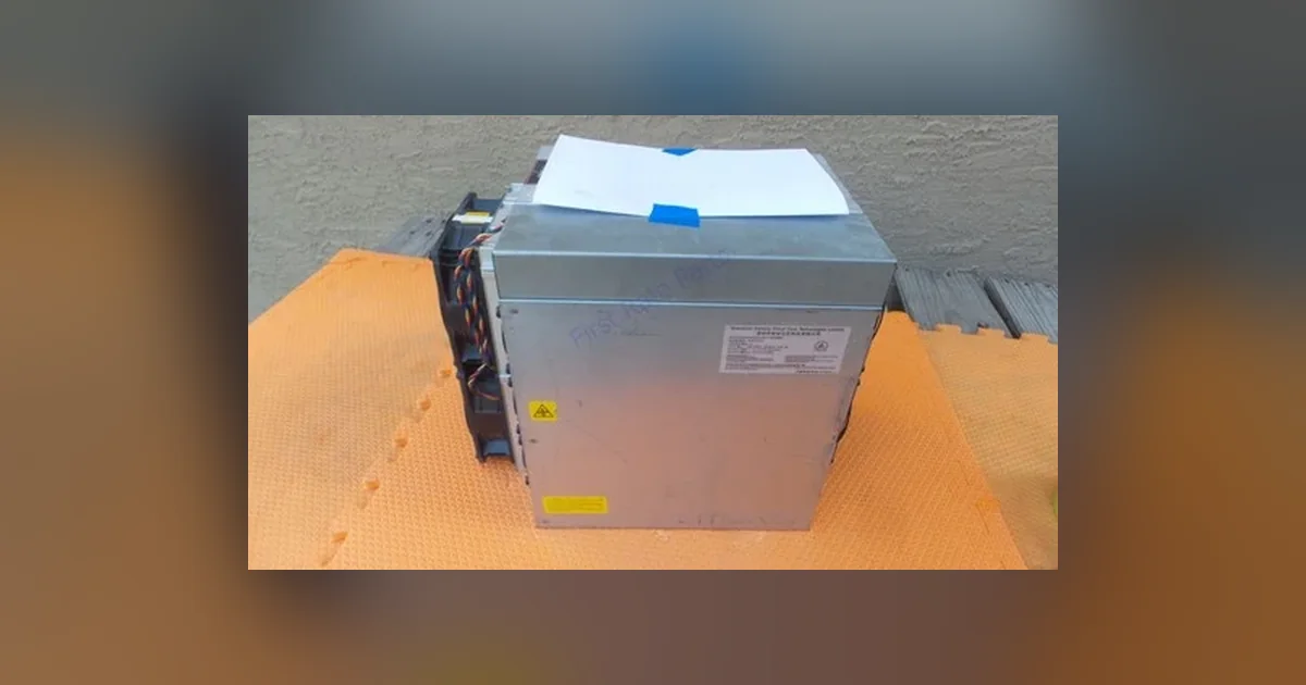 A Bitmain Antminer L9 Scrypt miner standing on an orange workshop mat, its ventilated steel case and end plate facing the camera.