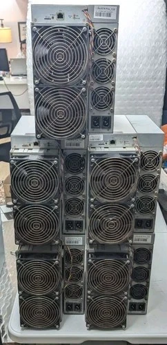 Five refurbished Antminer S19 units stacked in two tiers on a table, fan grilles facing forward and twin power inlets visible on the side of each machine.