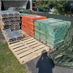 Used Antminer S19 miners banded and shrink-wrapped on wooden pallets outdoors, some under orange and green tarps.