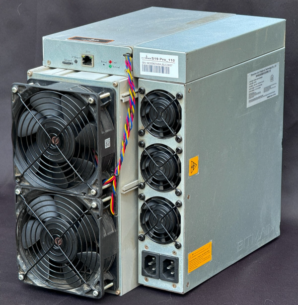 A used Bitmain Antminer S19 photographed from the intake side, showing the fan guard, the power supply mounted along the top of the chassis and the manufacturer label on the side panel.
