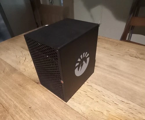 A VolcMiner D1 Mini on a wooden table: a black cube with a perforated front panel and rear logo plate.