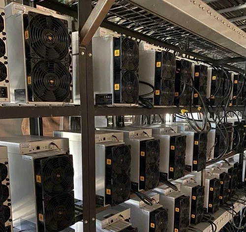 Two levels of a metal shelving rack packed end to end with Antminers seen from their fan faces, white power supplies sitting on top of each machine and cabling run along the frame of the rack.