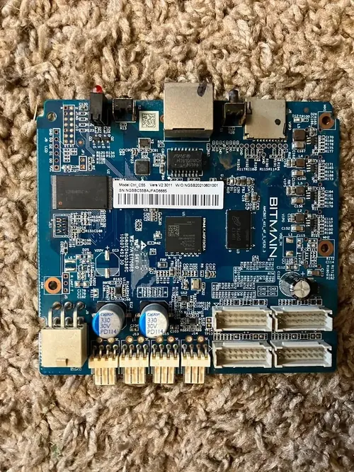 A blue Bitmain Antminer control board photographed on a carpet, two shielded network and USB sockets along its top edge, a BITMAIN silkscreen down the right side, a white barcode label reading Ctrl_C55, and rows of ribbon and multi-pin connectors along the bottom and right edges.